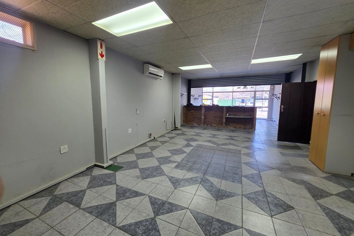 Open-plan retail space featuring tiled flooring, suspended ceiling with recessed lighting, air conditioning, and a built-in brick service counter with security shutter.