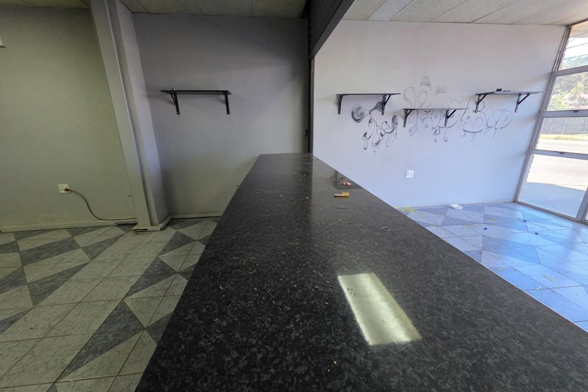 Empty retail space featuring a built-in counter, tiled flooring, and large storefront windows, requiring cosmetic updates and repairs to the walls and flooring.
