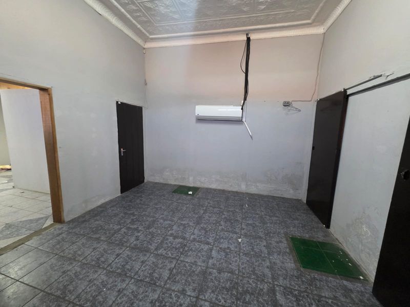 An empty retail or commercial space featuring tiled flooring, decorative ceiling details, and a wall-mounted air conditioning unit with visible wall surface wear.