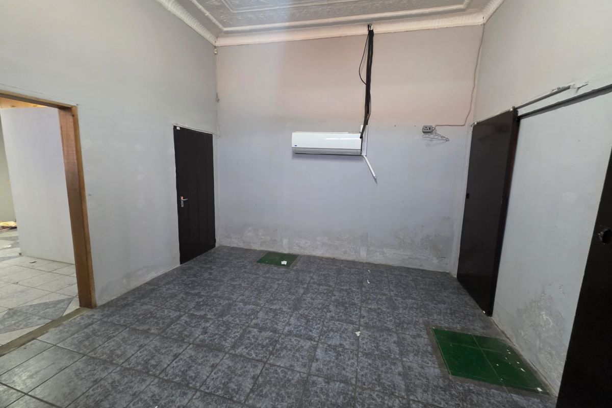 An empty retail or commercial space featuring tiled flooring, decorative ceiling details, and a wall-mounted air conditioning unit with visible wall surface wear.