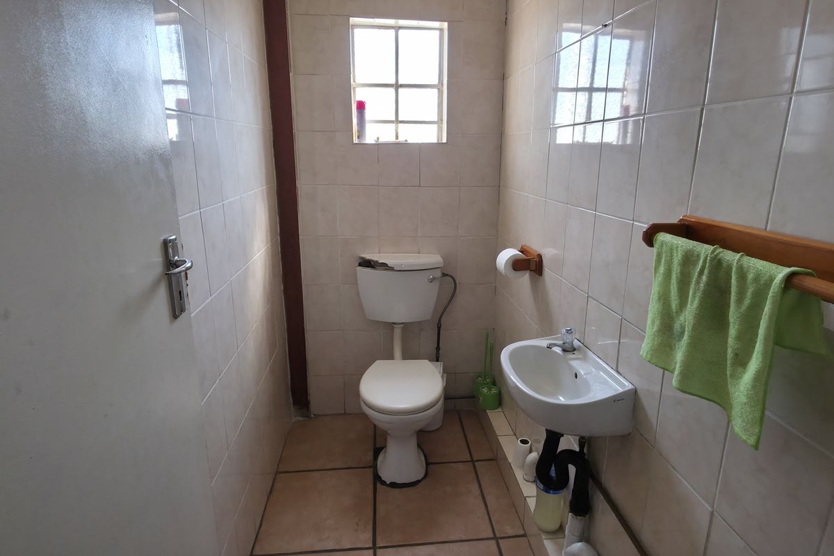 A compact industrial bathroom featuring tiled walls and floors, a wall-mounted basin, and a toilet with a damaged cistern lid.