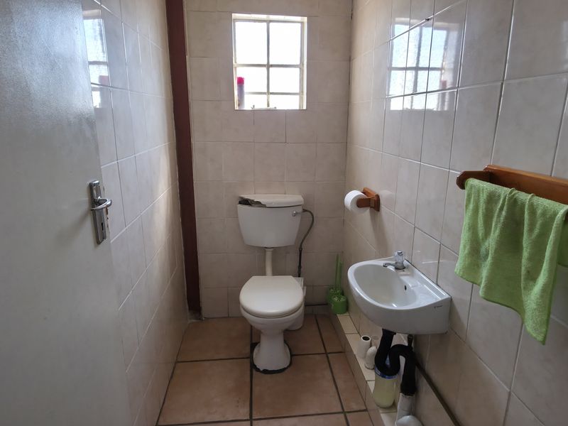 A compact industrial bathroom featuring tiled walls and floors, a wall-mounted basin, and a toilet with a damaged cistern lid.