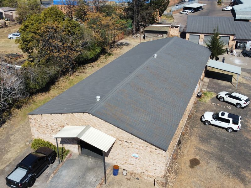 Aerial view of an industrial warehouse building featuring a corrugated metal roof, brick exterior, and paved driveway access.