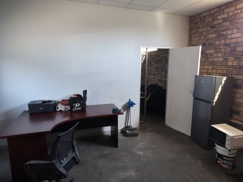 Industrial office space featuring exposed brick walls, concrete flooring, and a suspended ceiling, providing a functional workspace environment.
