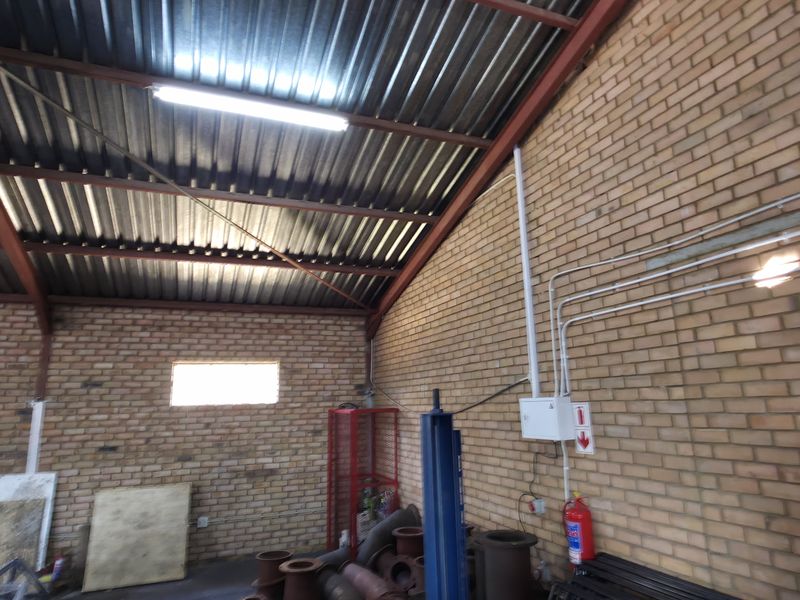 Spacious industrial utility area featuring exposed brick walls, high corrugated metal roofing, and functional overhead fluorescent lighting.