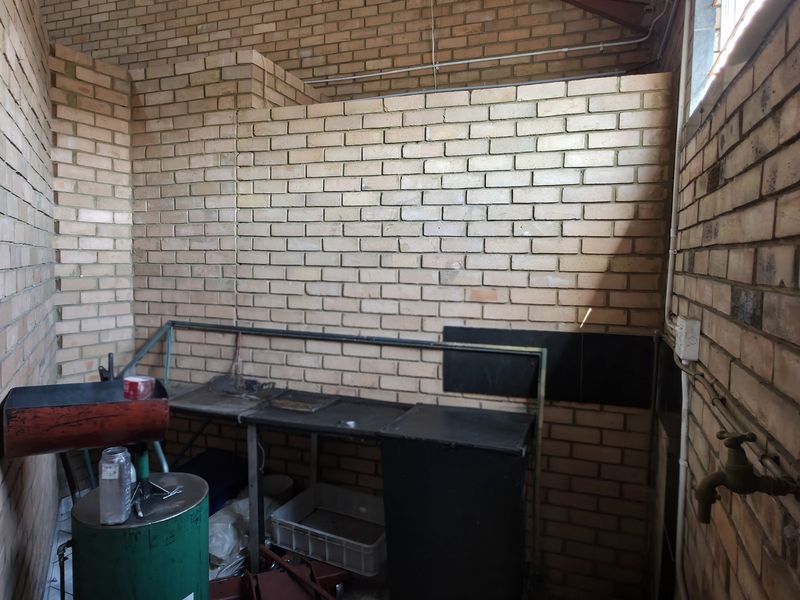 A utilitarian industrial space featuring exposed brick walls, a wall-mounted tap, and a metal workbench, suitable for workshop or storage use.