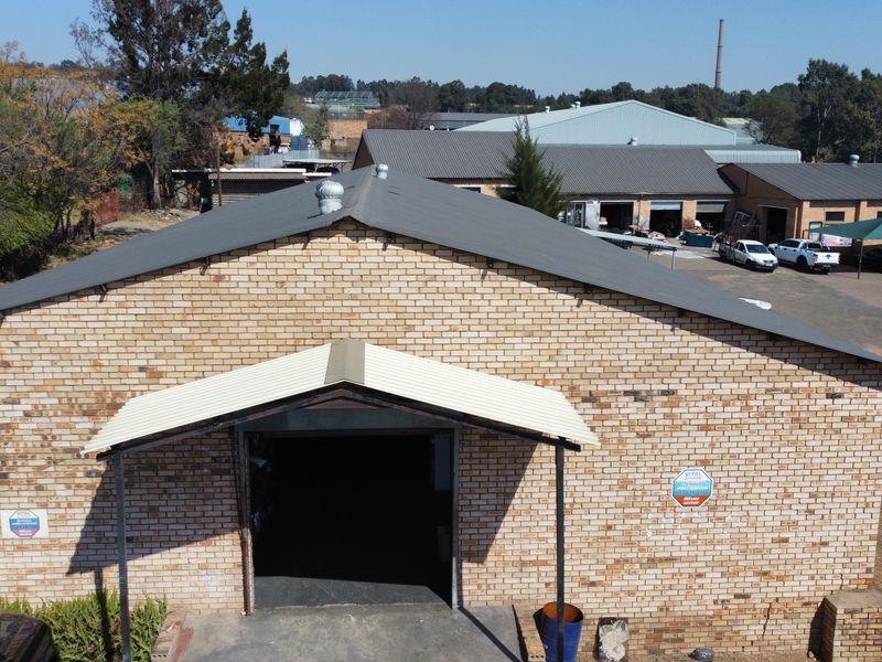 Aerial view of an industrial warehouse building featuring a brick facade, pitched metal roof, and a covered entrance with a large roller door.