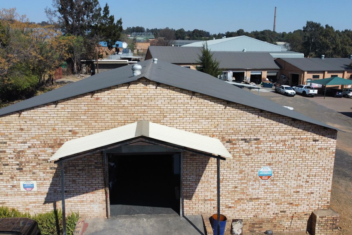 Aerial view of an industrial warehouse building featuring a brick facade, pitched metal roof, and a covered entrance with a large roller door.