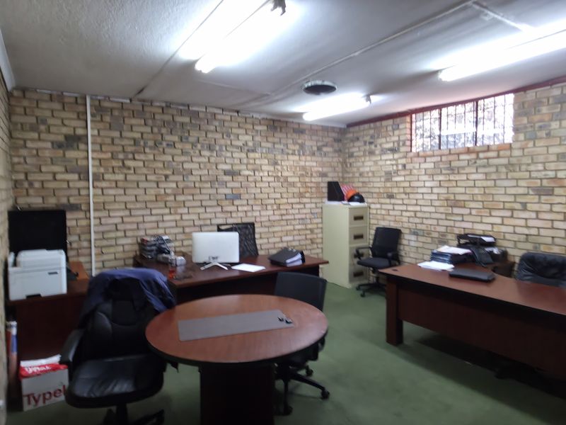 Functional office space featuring exposed brick walls, fluorescent lighting, and security-barred windows, suitable for a professional industrial or commercial workspace.