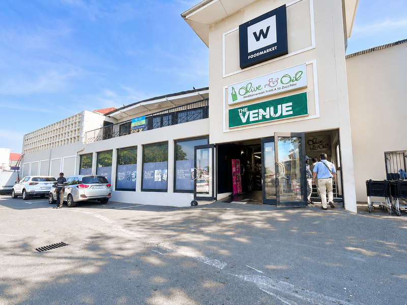 Front exterior view of a commercial office and retail building featuring prominent signage, paved parking, and a glass-fronted entrance.