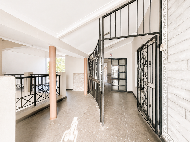 A secure office entrance featuring tiled flooring, wrought iron security gates, and structural columns leading to a glass-panelled doorway.