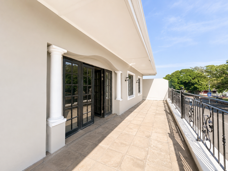 A spacious covered balcony featuring tiled flooring, decorative columns, and a wrought iron balustrade, providing an elegant outdoor transition space.