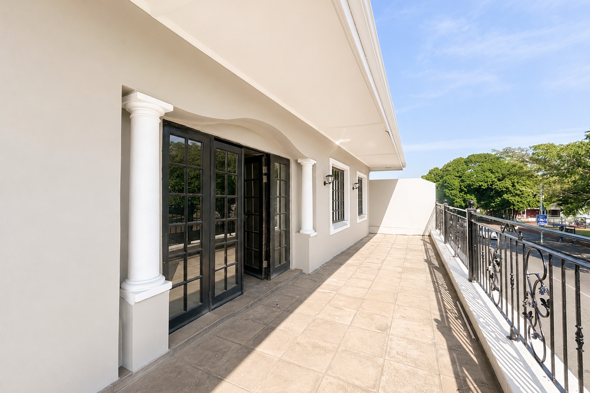 A spacious covered balcony featuring tiled flooring, decorative columns, and a wrought iron balustrade, providing an elegant outdoor transition space.