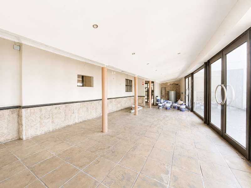 Spacious, empty office area featuring tiled flooring, structural columns, and large glass sliding doors providing ample natural light.