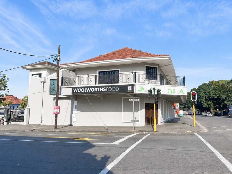 A prominent corner office building featuring a tiled roof, a wrap-around balcony with wrought iron railings, and established commercial signage.