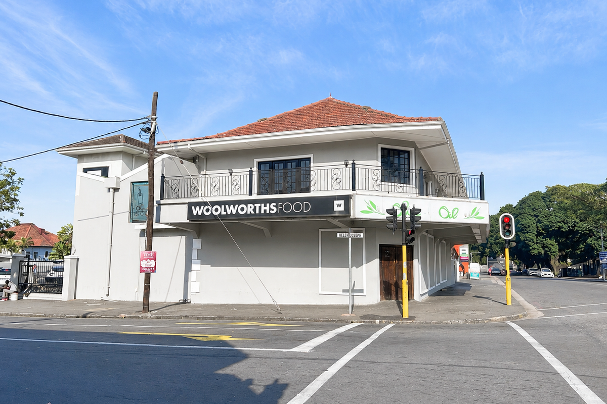 A prominent corner office building featuring a tiled roof, a wrap-around balcony with wrought iron railings, and established commercial signage.