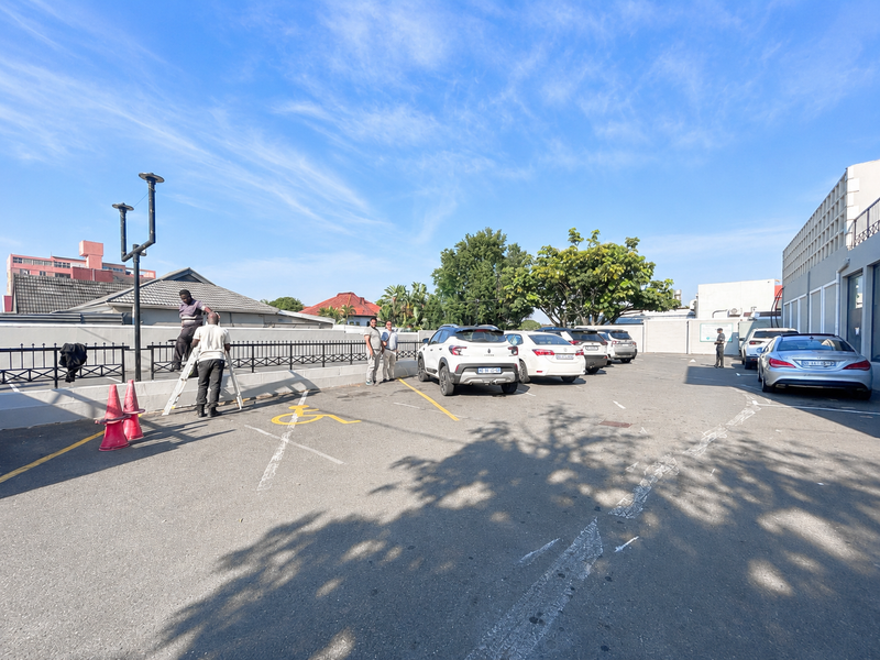An outdoor paved parking area featuring designated bays, perimeter metal fencing, and exterior lighting infrastructure.