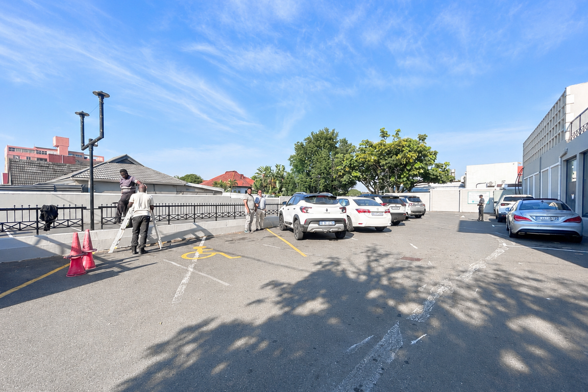 An outdoor paved parking area featuring designated bays, perimeter metal fencing, and exterior lighting infrastructure.