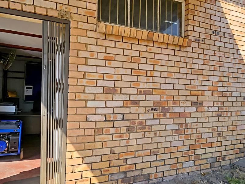 Exterior view of an industrial building featuring a face brick facade, security gate, and fixed windows with burglar bars.