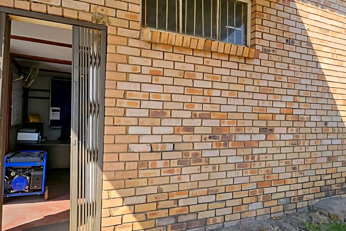 Exterior view of an industrial building featuring a face brick facade, security gate, and fixed windows with burglar bars.
