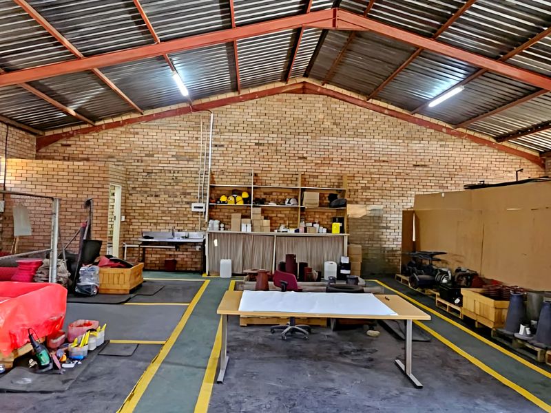 Spacious industrial utility area featuring exposed brick walls, high steel truss ceilings, and durable concrete flooring, suitable for workshop or storage operations.