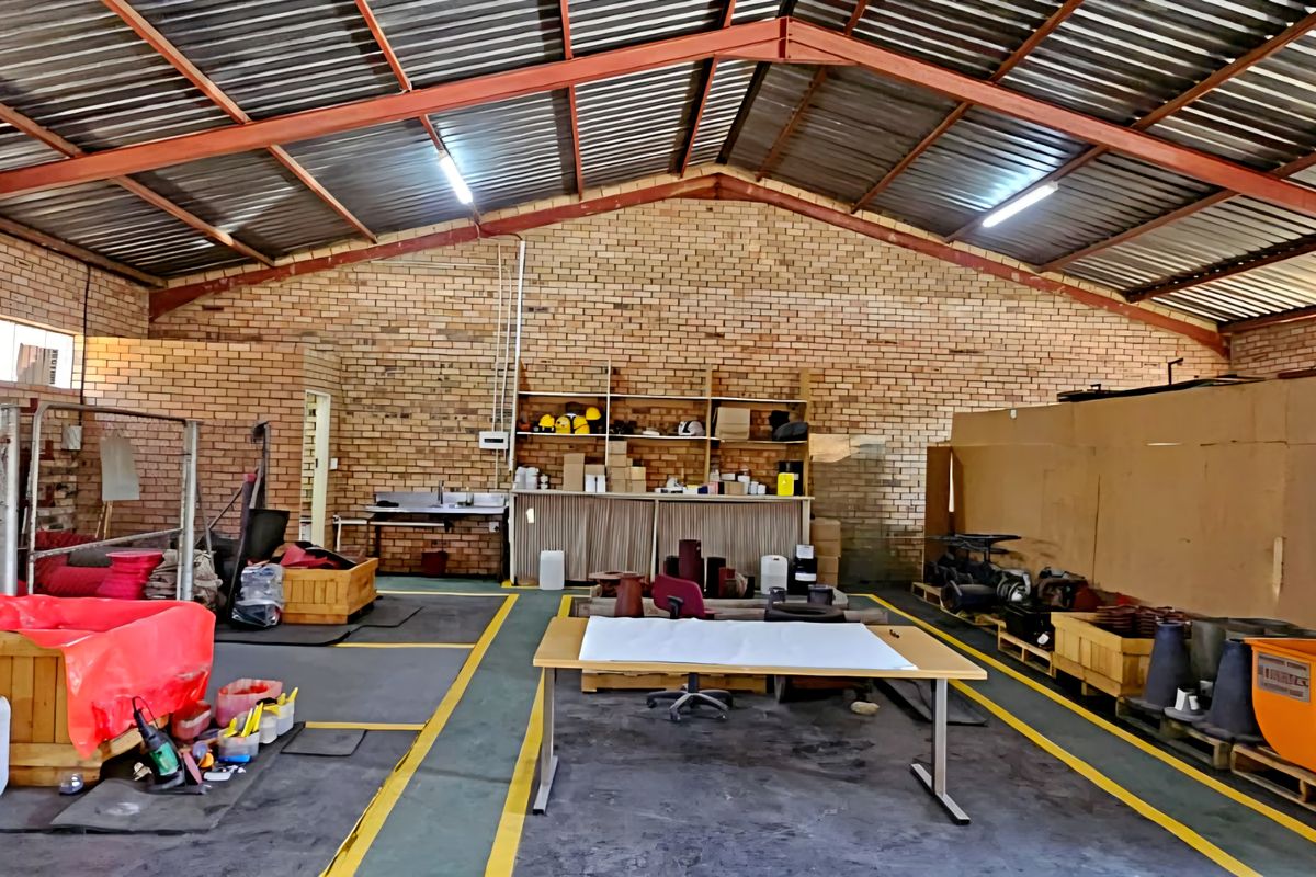 Spacious industrial utility area featuring exposed brick walls, high steel truss ceilings, and durable concrete flooring, suitable for workshop or storage operations.