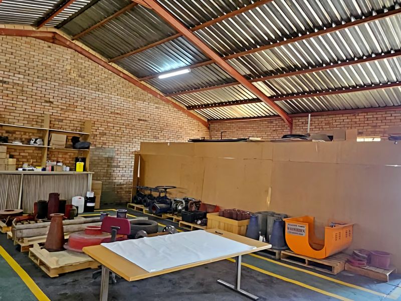 Spacious industrial utility area featuring exposed brick walls, high corrugated metal roofing, steel trusses, and a built-in stainless steel sink with roller door access.