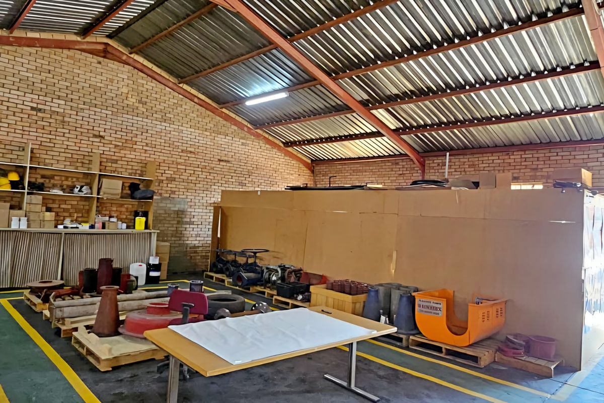 Spacious industrial utility area featuring exposed brick walls, high corrugated metal roofing, steel trusses, and a built-in stainless steel sink with roller door access.