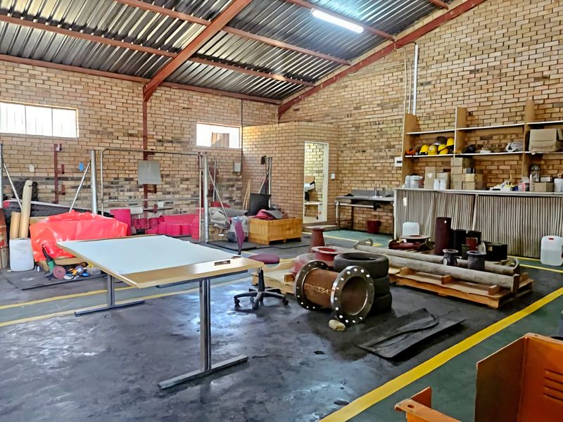 Spacious industrial utility area featuring exposed brick walls, high corrugated metal roofing with steel trusses, and durable concrete flooring with painted safety markings.