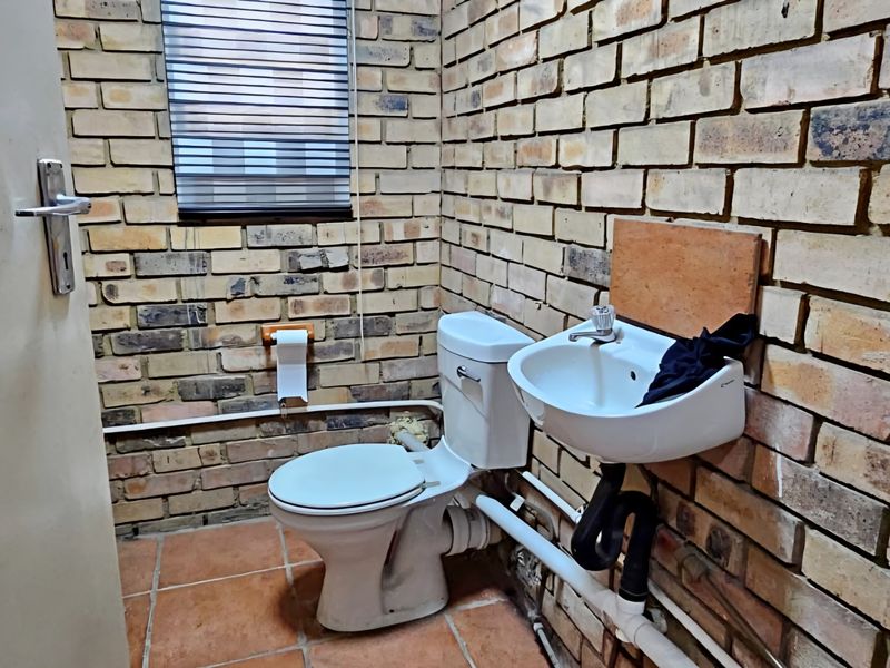A compact industrial-style bathroom featuring exposed brick walls, ceramic tile flooring, a wall-mounted basin, and a standard toilet.
