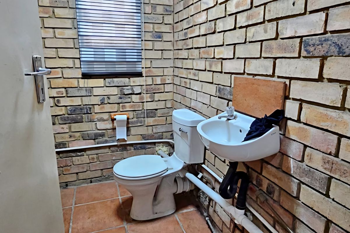 A compact industrial-style bathroom featuring exposed brick walls, ceramic tile flooring, a wall-mounted basin, and a standard toilet.