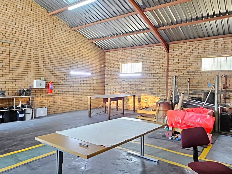 Spacious industrial garage featuring exposed brick walls, high corrugated metal ceilings, fluorescent lighting, and durable concrete flooring suitable for workshop or storage use.