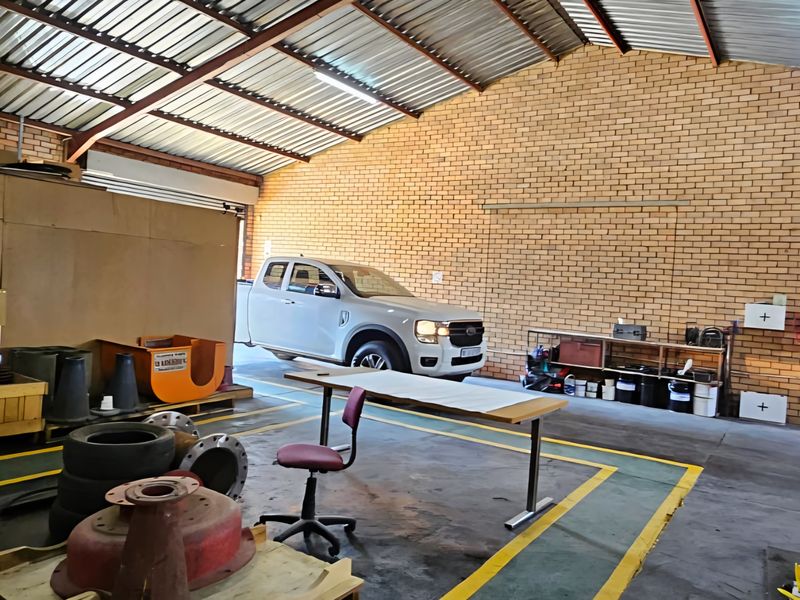 Spacious industrial utility area featuring exposed brick walls, high corrugated metal roofing, and durable concrete flooring, suitable for workshop or storage use.