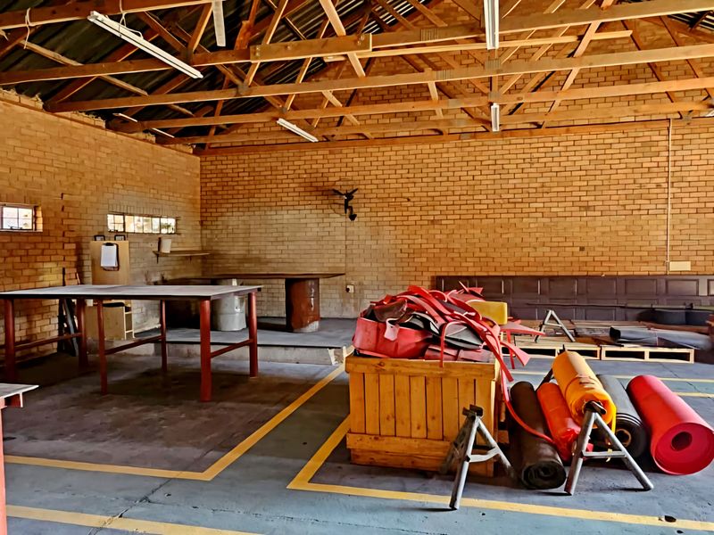 Spacious industrial utility area featuring exposed brick walls, timber roof trusses, concrete flooring, and a large roller shutter door for easy access.