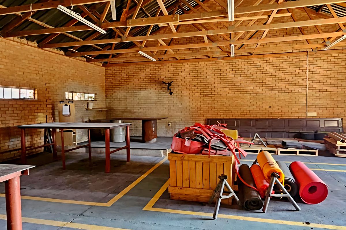 Spacious industrial utility area featuring exposed brick walls, timber roof trusses, concrete flooring, and a large roller shutter door for easy access.