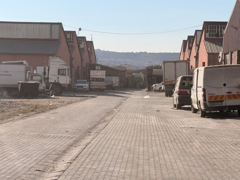 View of an industrial complex access road lined with warehouse buildings and paved surfaces.