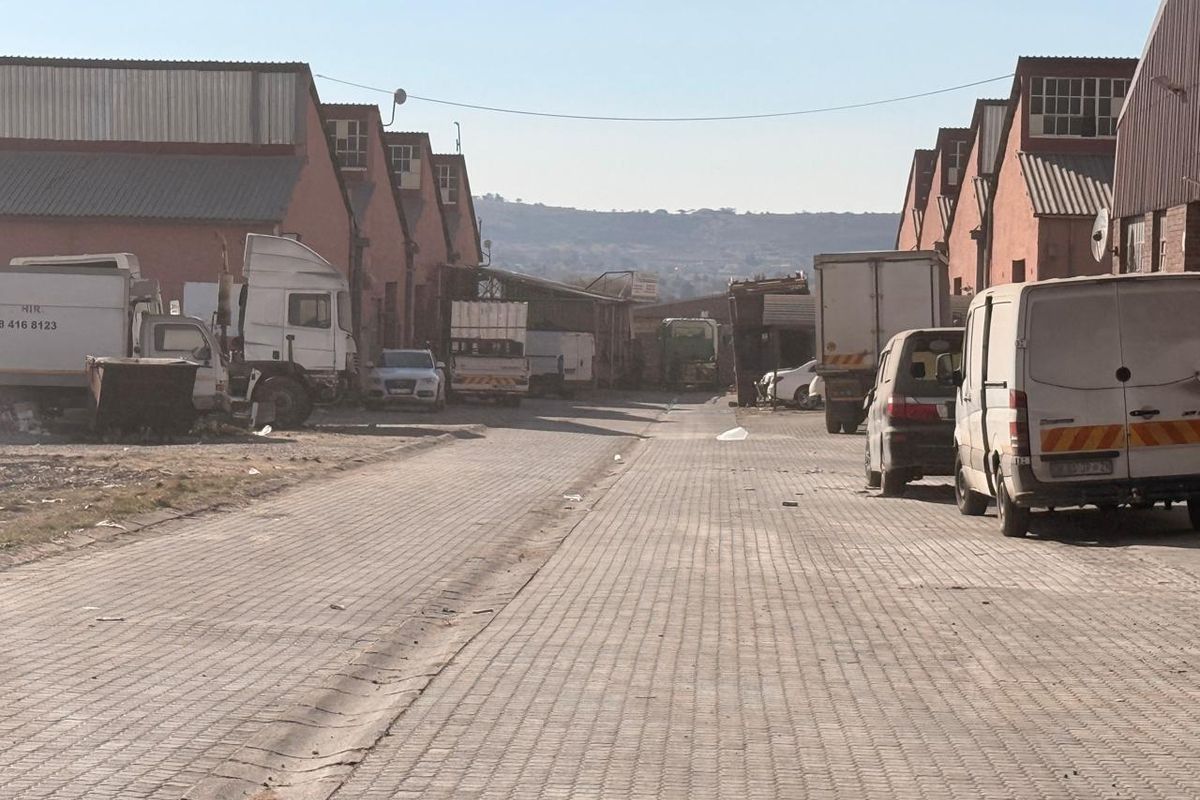 View of an industrial complex access road lined with warehouse buildings and paved surfaces.