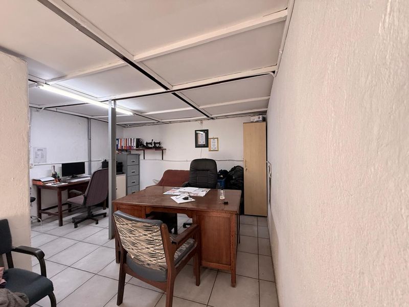A functional commercial office space featuring tiled flooring, a suspended ceiling with integrated lighting, and a built-in storage cupboard.