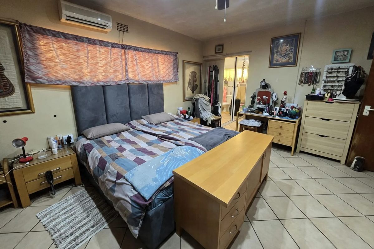 Spacious bedroom featuring tiled flooring, an integrated air conditioning unit, and direct access to an en-suite bathroom through a sliding door.
