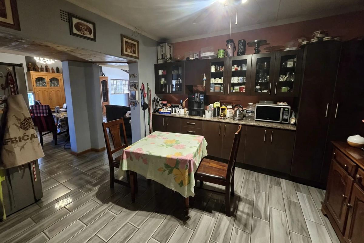 A functional kitchen featuring dark wood cabinetry, granite countertops, and modern grey tiled flooring, with an open-plan layout connecting to the adjacent living area.