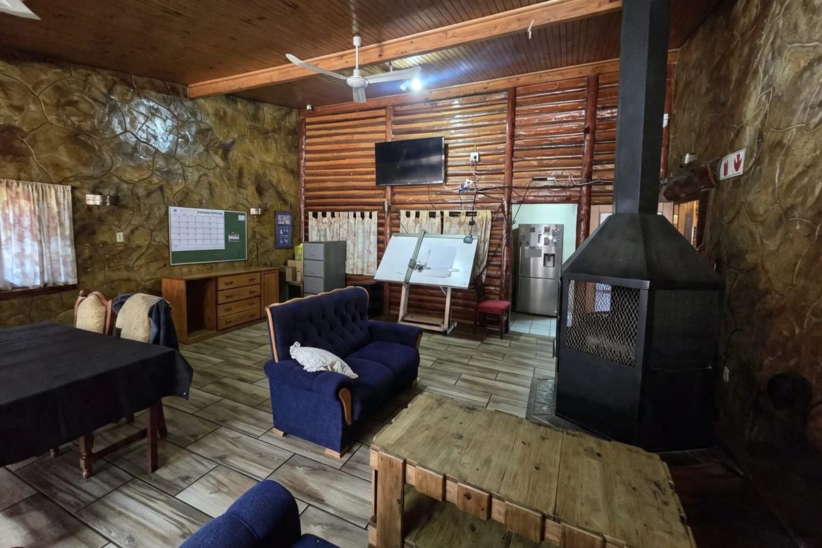 Spacious living area featuring a prominent freestanding fireplace, timber-clad ceilings, and a mix of stone and log-style wall finishes with tiled flooring.