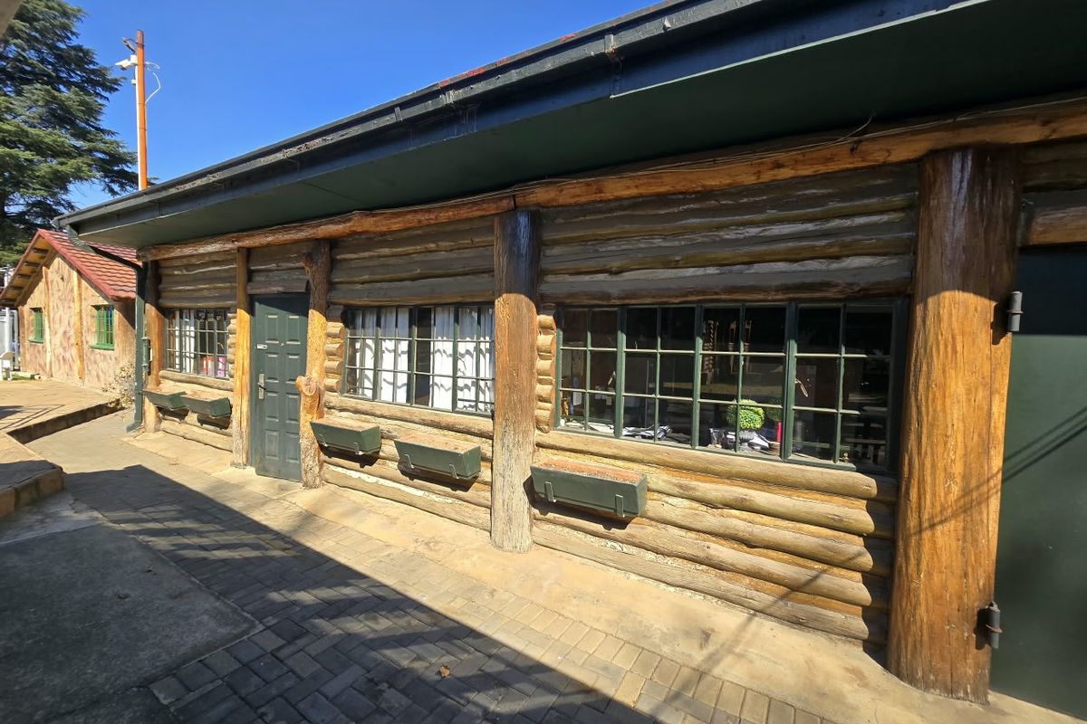 Exterior view of a rustic log cabin style building featuring timber walls, grid-pattern windows, and a paved walkway.