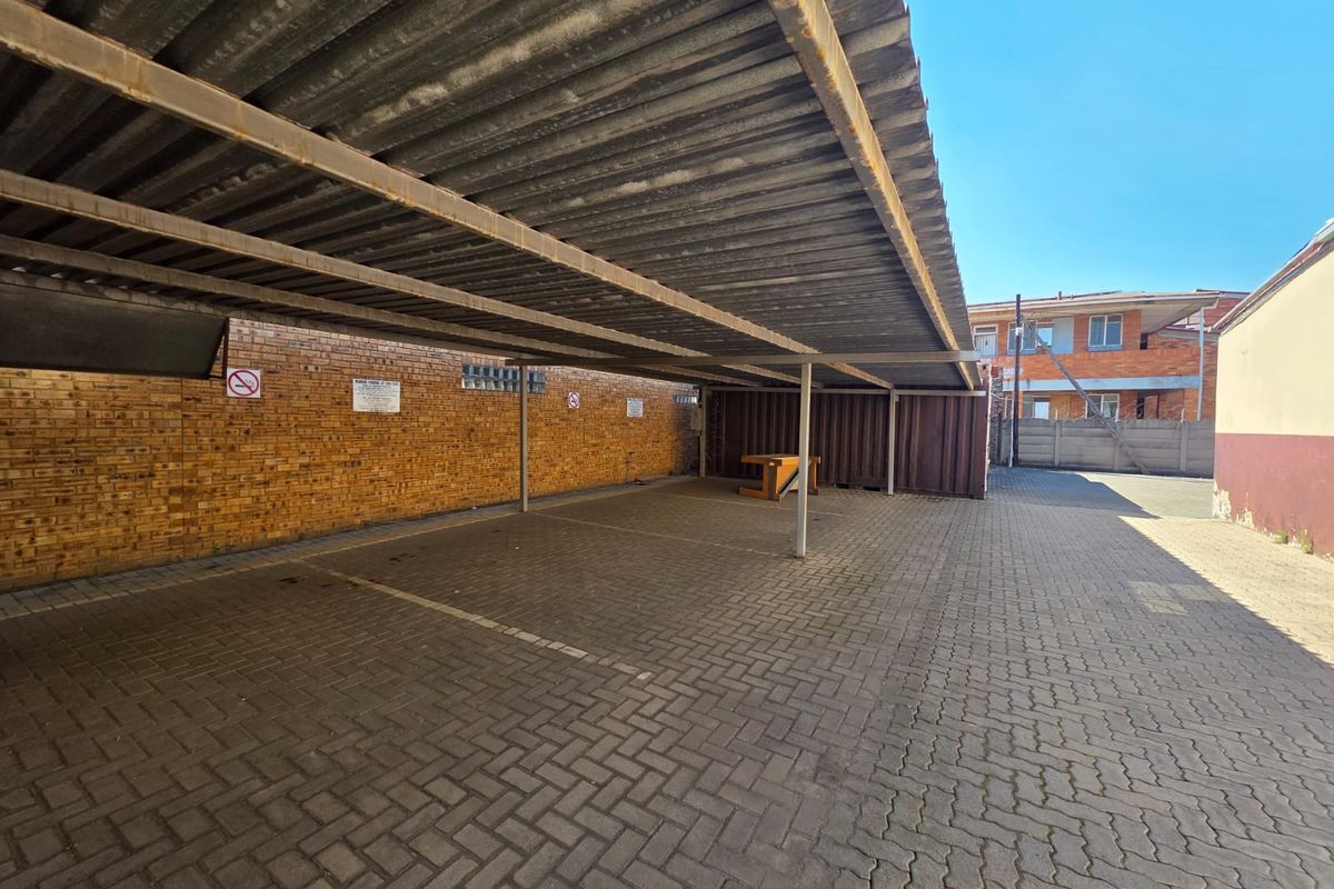 A covered outdoor parking area featuring a corrugated metal roof, brick boundary walls, and paved flooring, suitable for multiple vehicles.