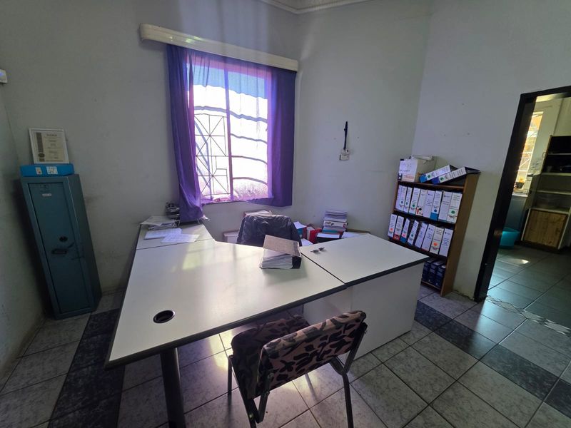 A functional office space featuring tiled flooring and a window with security bars, currently utilized as a workspace.