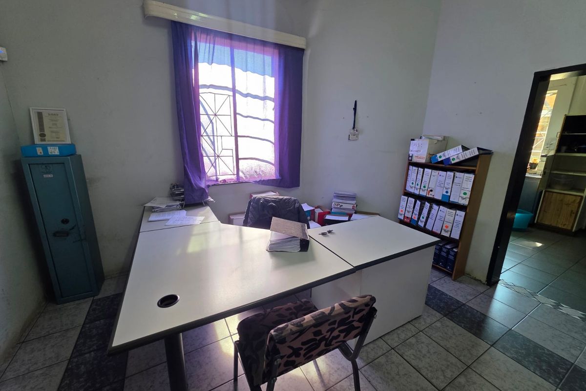 A functional office space featuring tiled flooring and a window with security bars, currently utilized as a workspace.