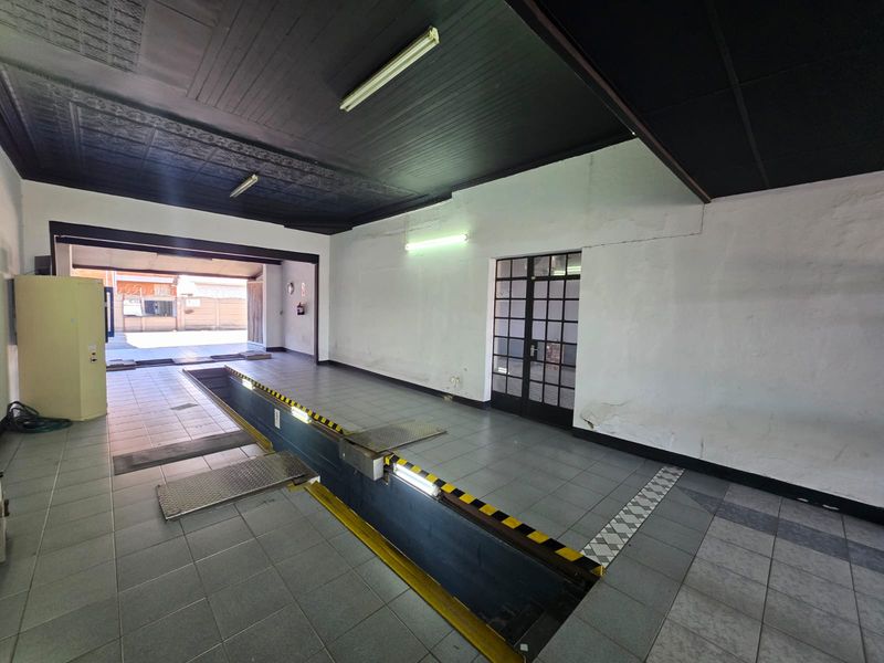 A spacious commercial garage featuring a built-in vehicle inspection pit, tiled flooring, and fluorescent lighting, suitable for automotive service or workshop use.