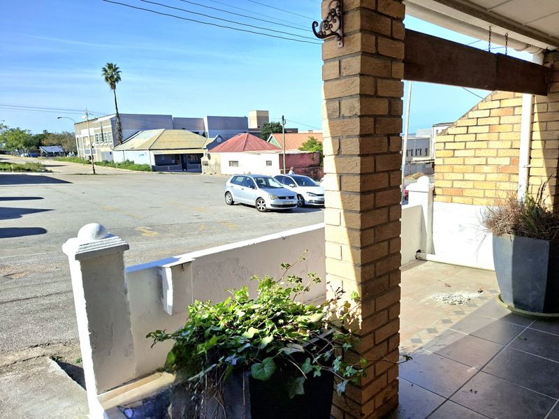 A covered patio area featuring brick pillars and tiled flooring, overlooking a street-level parking area.