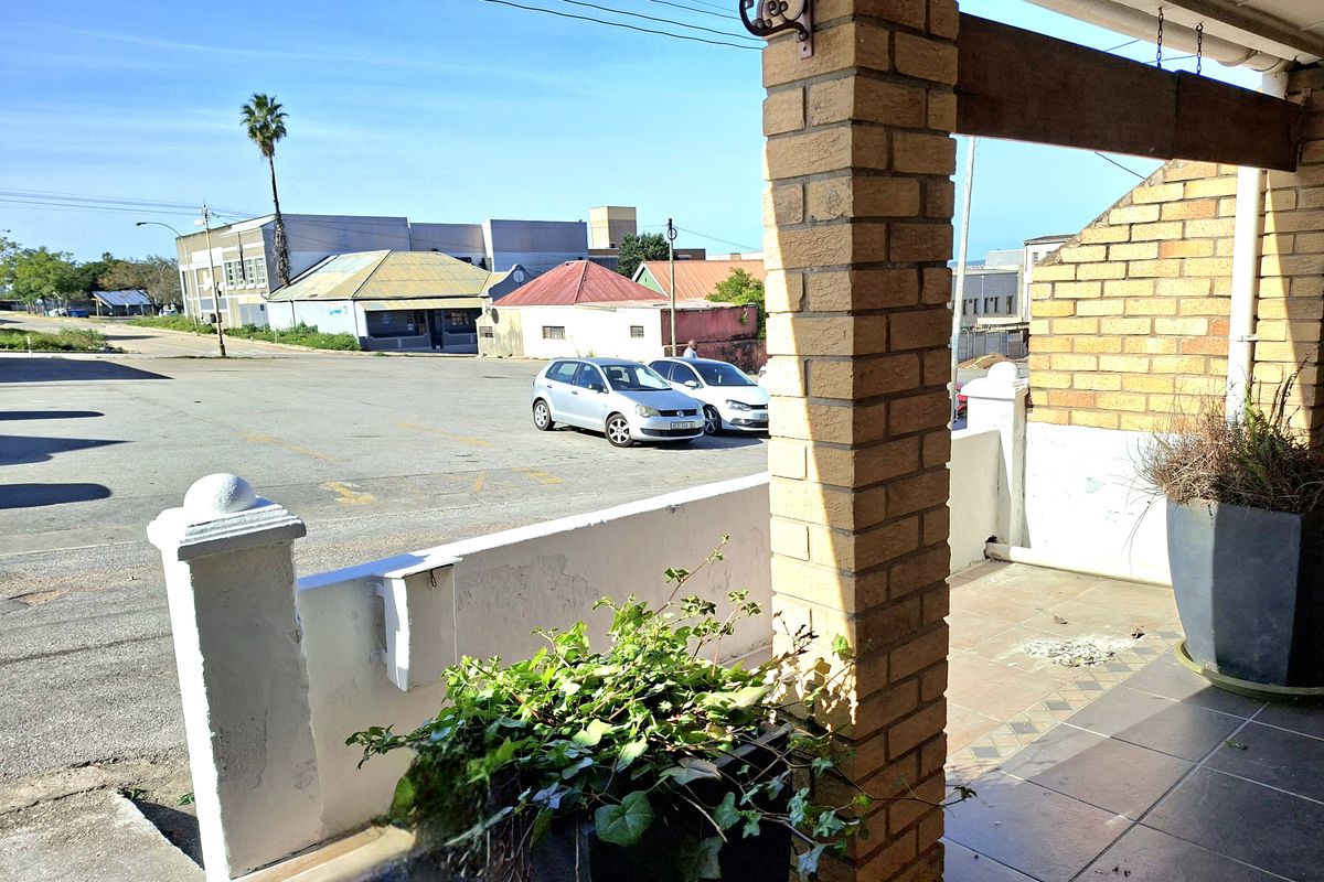 A covered patio area featuring brick pillars and tiled flooring, overlooking a street-level parking area.