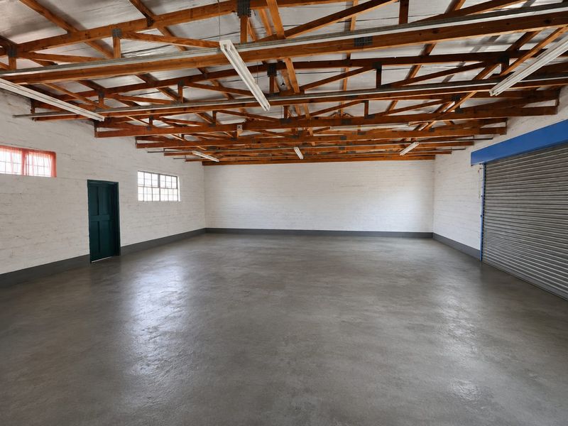 Spacious open-plan garage or utility space featuring exposed timber roof trusses, polished concrete flooring, and a secure roller shutter door.