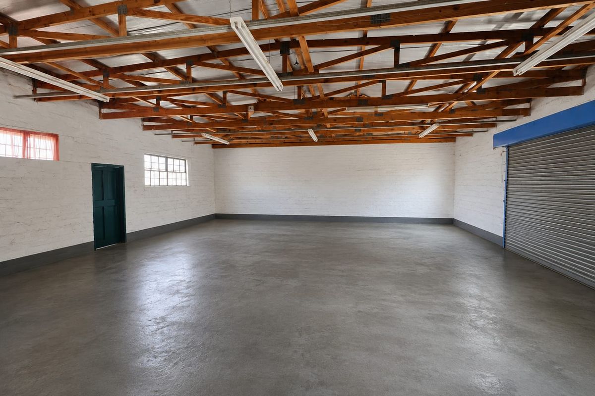 Spacious open-plan garage or utility space featuring exposed timber roof trusses, polished concrete flooring, and a secure roller shutter door.